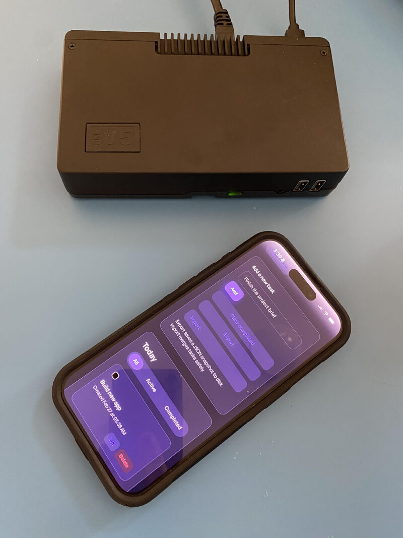 Black OurBox device and a smartphone showing a dark to-do app dashboard on a blue tabletop.
